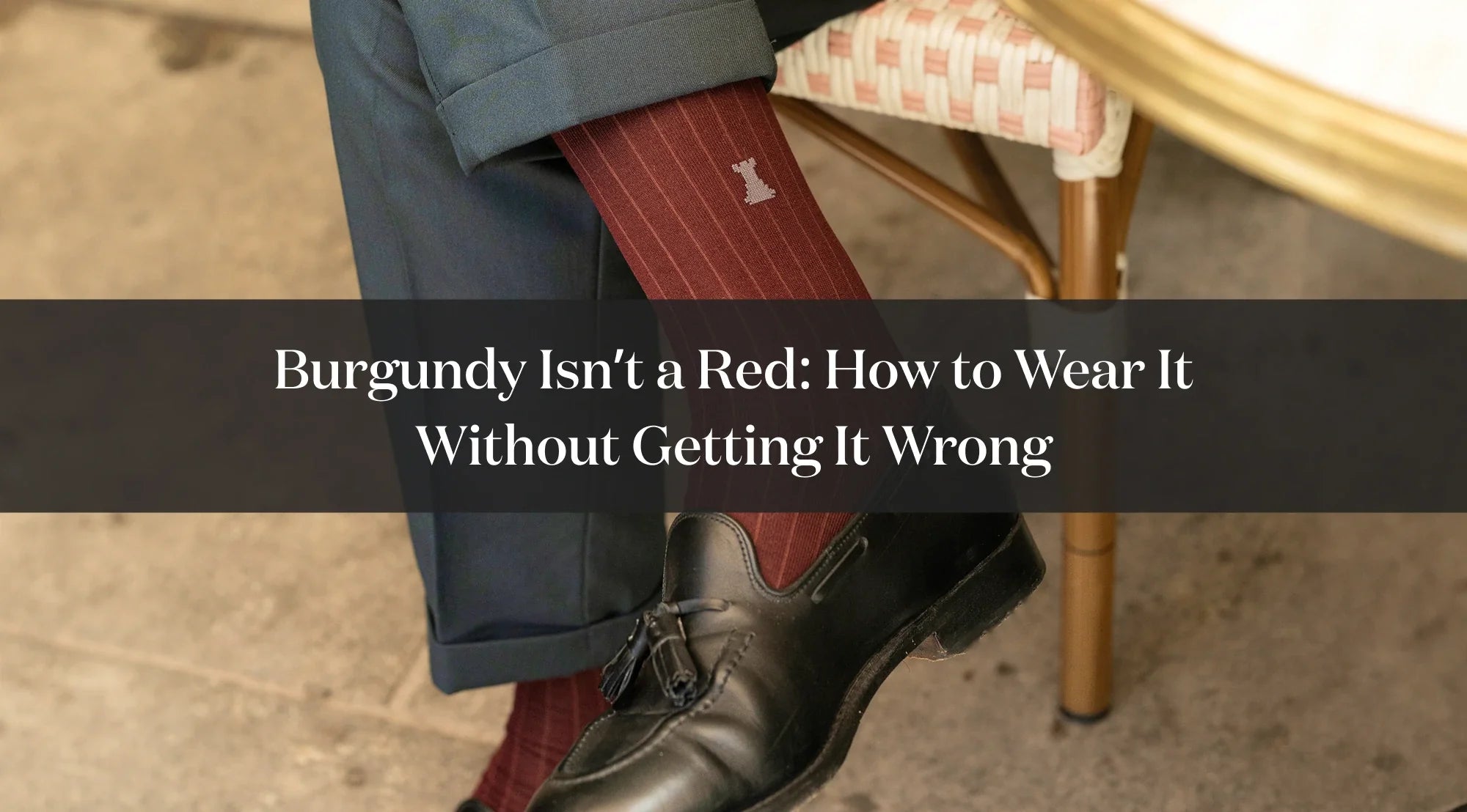 Detail of a burgundy sock worn with a black dress shoe and blue trousers, with text about how to style burgundy.