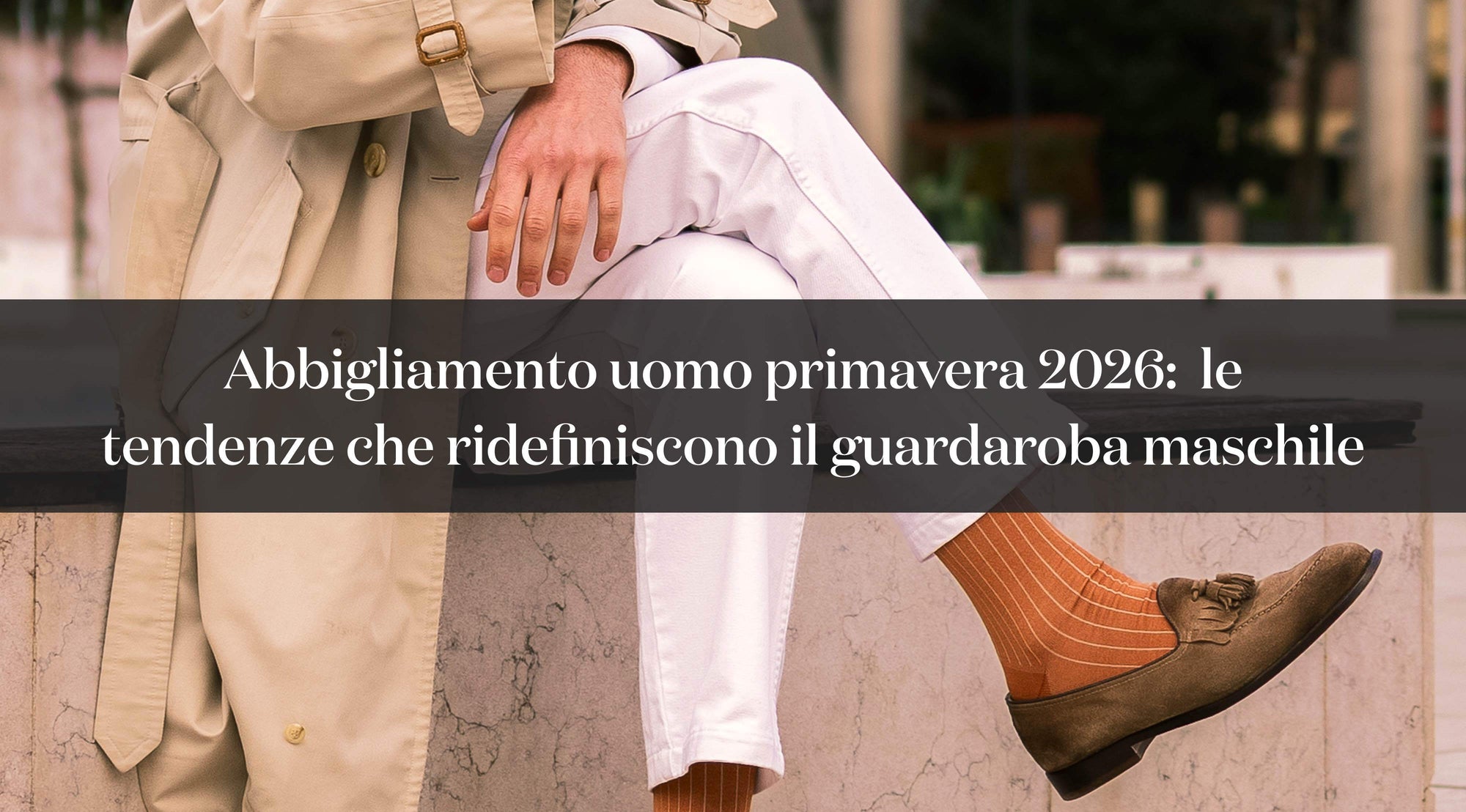 Look uomo primavera 2026 con trench beige, pantaloni bianchi e scarpe marroni in camoscio.